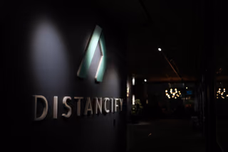 The illuminated Distancify symbol and wordmark on a dark wall beside the office corridor.